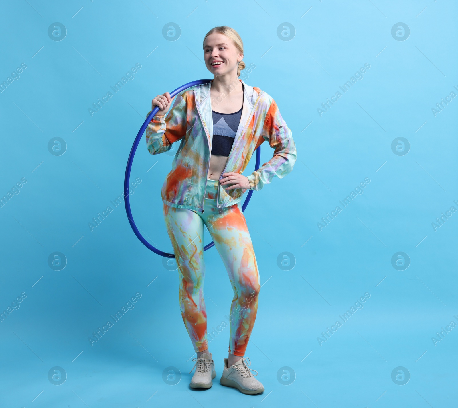 Photo of Beautiful young woman with hula hoop on light blue background, space for text