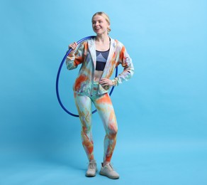 Photo of Beautiful young woman with hula hoop on light blue background, space for text