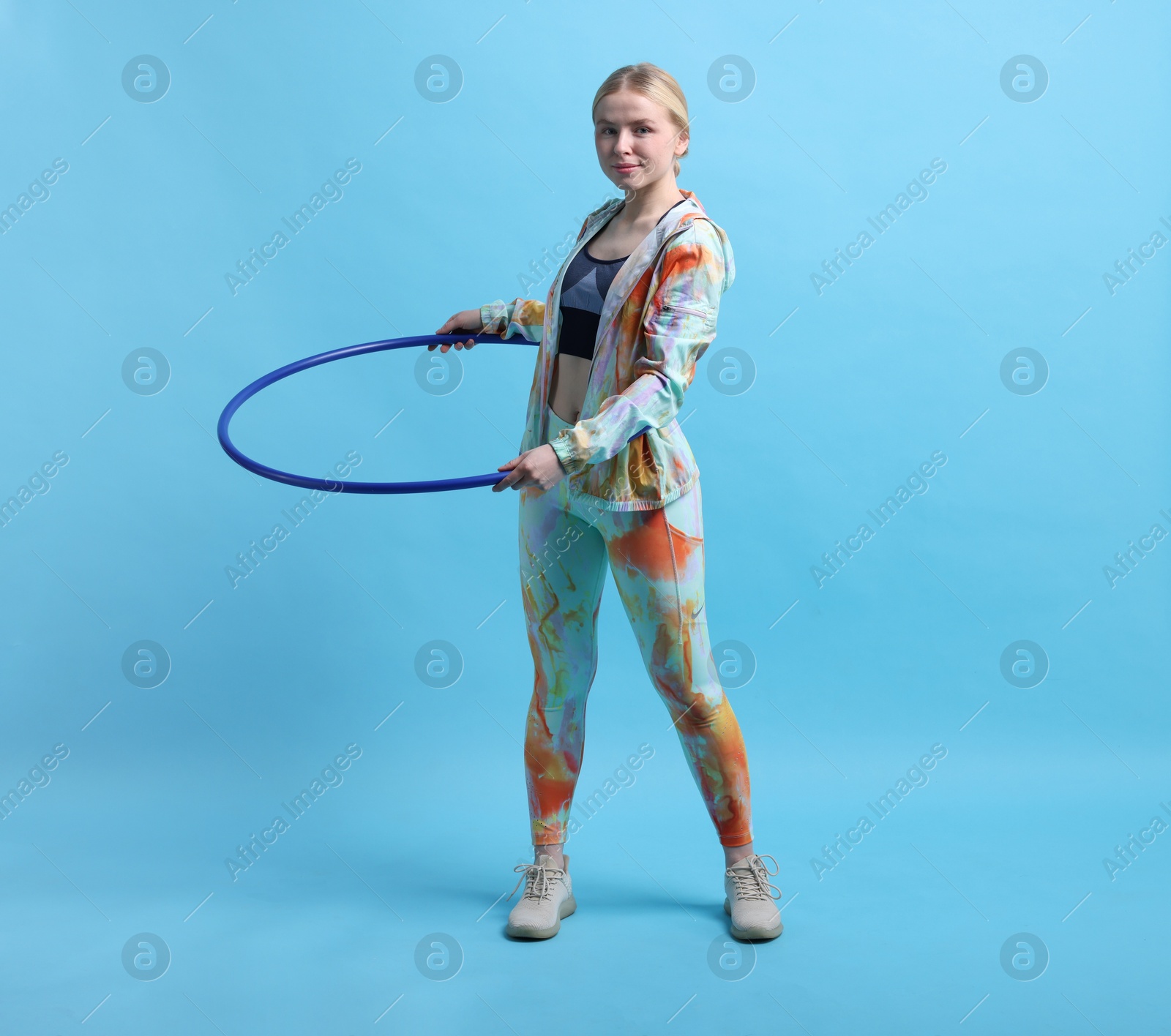 Photo of Beautiful young woman exercising with hula hoop on light blue background