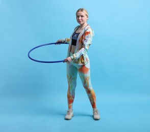 Photo of Beautiful young woman exercising with hula hoop on light blue background