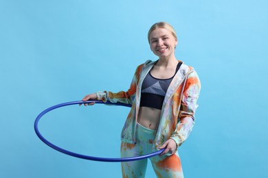 Beautiful young woman exercising with hula hoop on light blue background