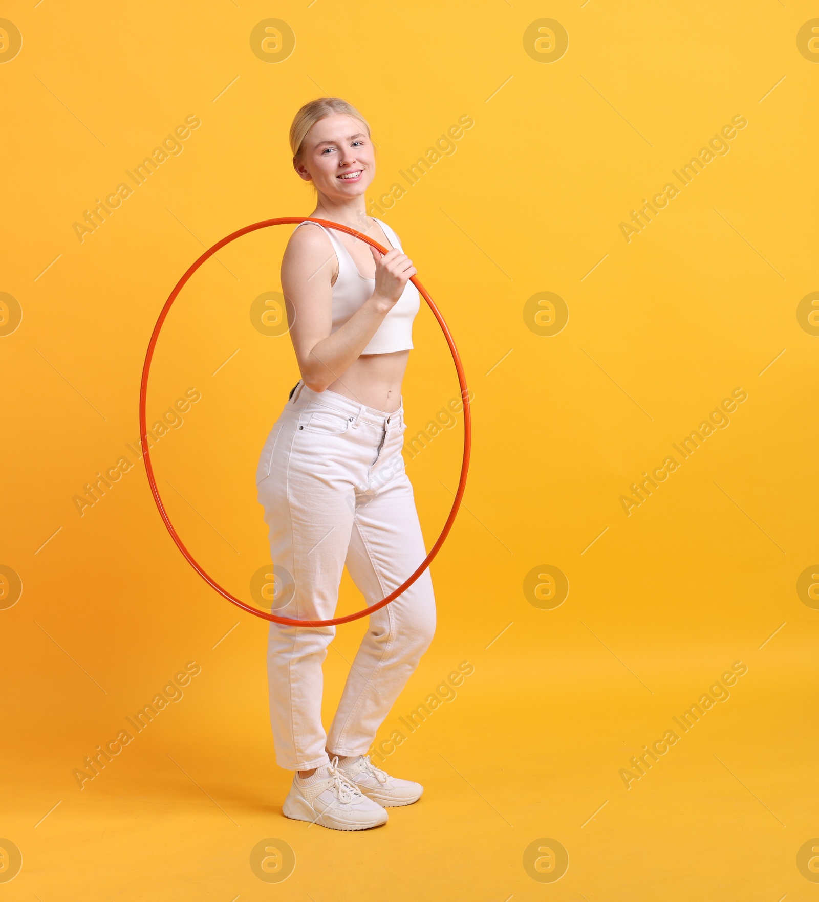 Photo of Beautiful young woman with hula hoop on yellow background, space for text