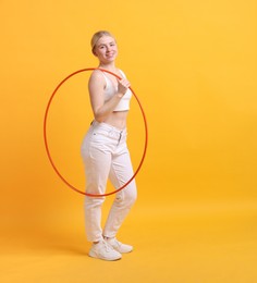 Photo of Beautiful young woman with hula hoop on yellow background, space for text