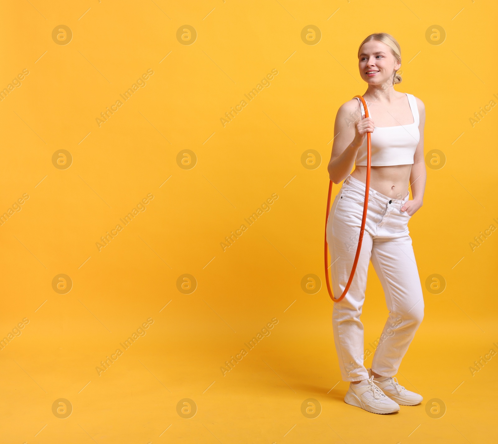 Photo of Beautiful young woman with hula hoop on yellow background, space for text