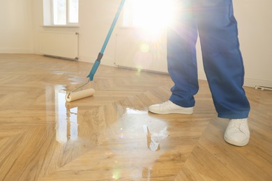 Photo of Man polishing parquet with varnish indoors, closeup