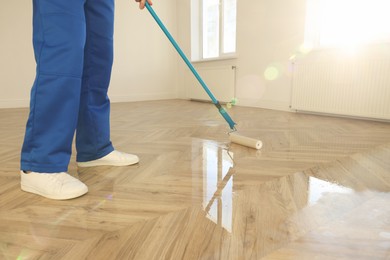 Photo of Man polishing parquet with varnish indoors, closeup