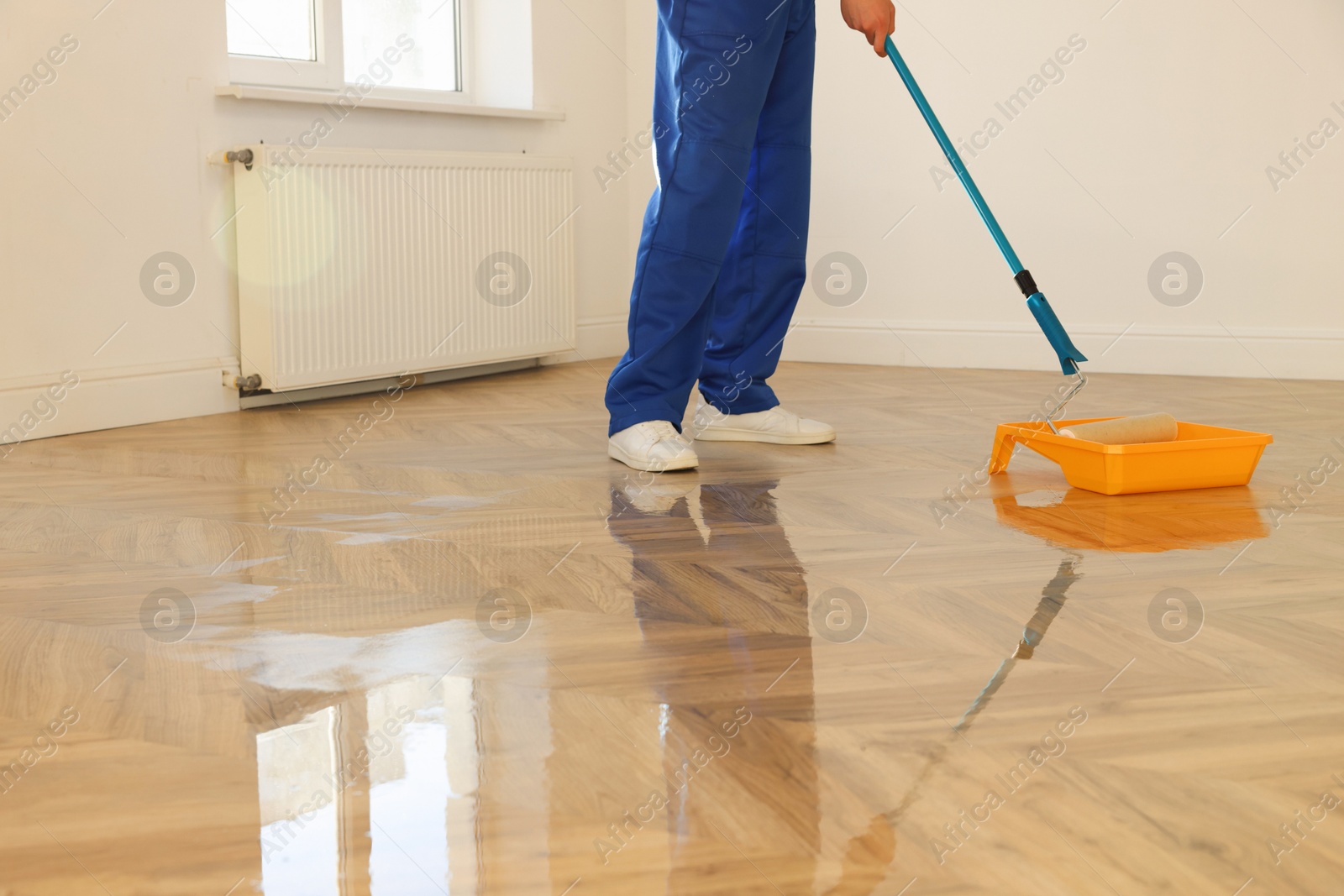 Photo of Process of polishing. Man dipping roller into tray with varnish indoors, closeup