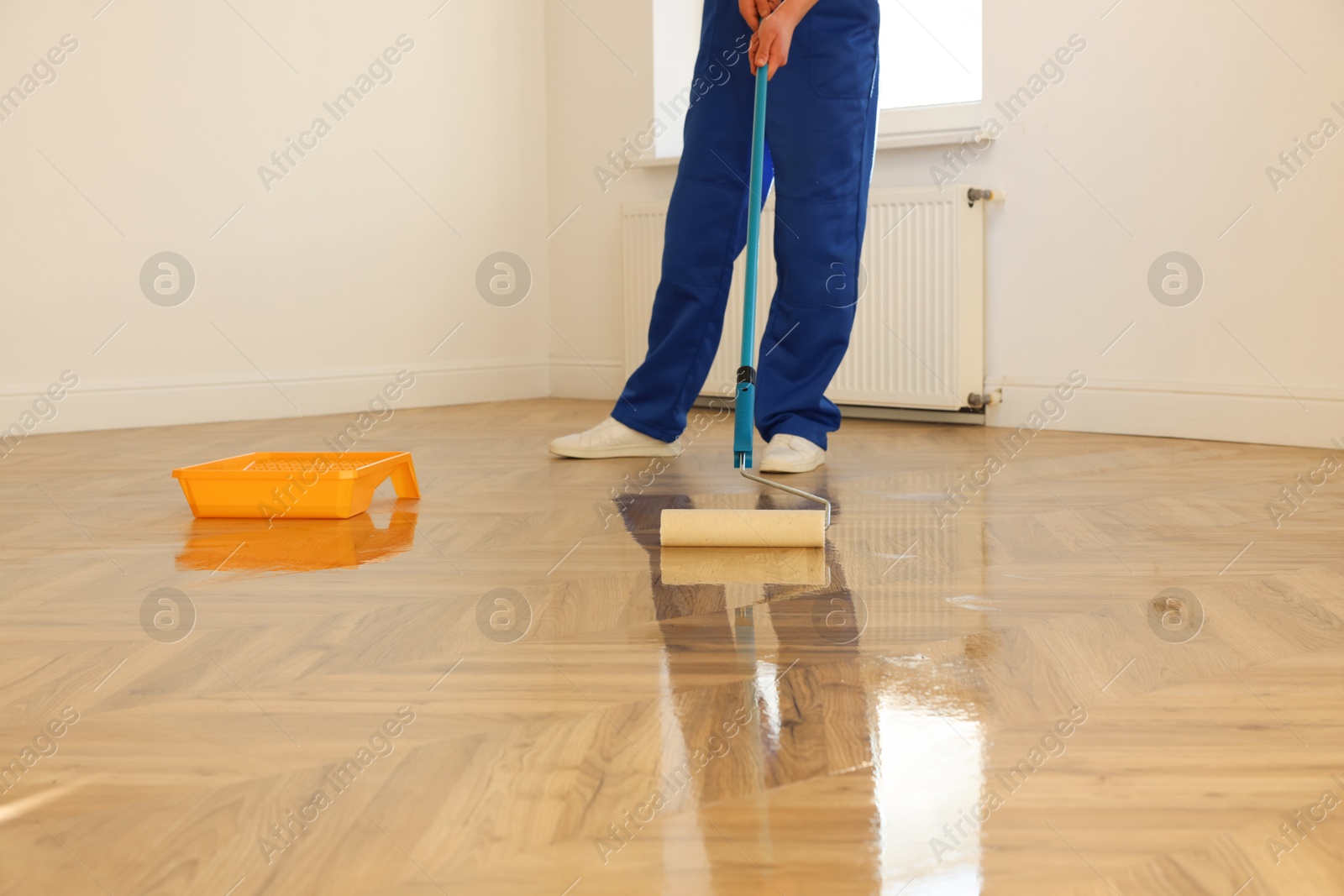 Photo of Man polishing parquet with varnish indoors, closeup