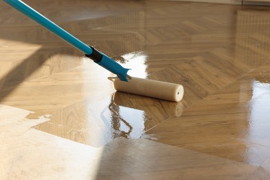 Photo of Polishing parquet with roller and varnish indoors, closeup