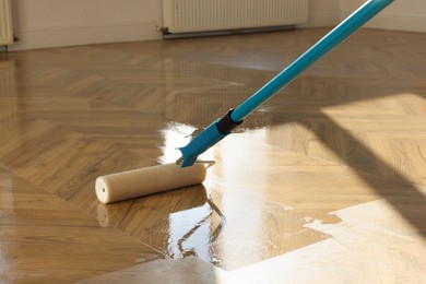 Photo of Polishing parquet with roller and varnish indoors, closeup