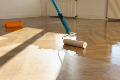 Photo of Polishing parquet with roller and varnish indoors, closeup