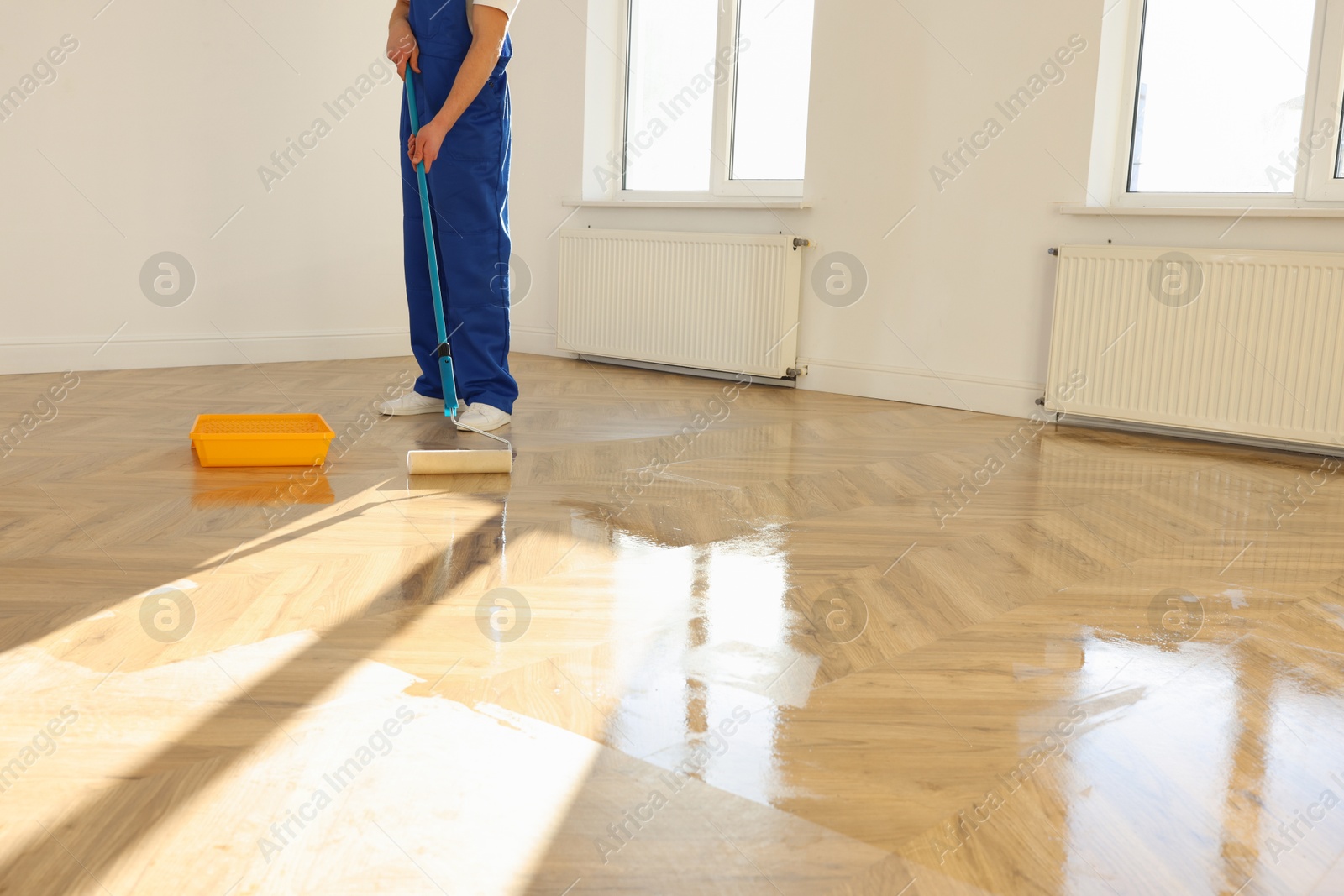 Photo of Man polishing parquet with varnish indoors, closeup