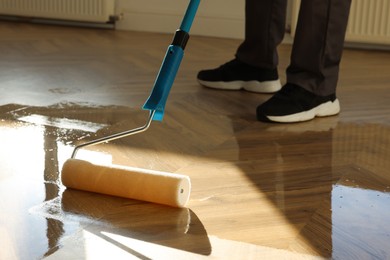 Photo of Man polishing parquet with varnish indoors, closeup