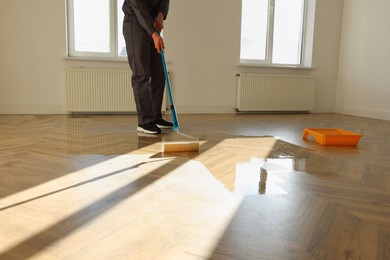 Photo of Man polishing parquet with varnish indoors, closeup