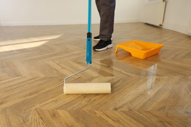 Photo of Man polishing parquet with varnish indoors, closeup