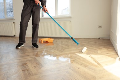 Photo of Man polishing parquet with varnish indoors, closeup