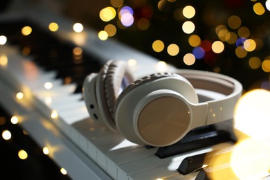 Photo of Headphones on electric piano against blurred lights, closeup. Bokeh effect