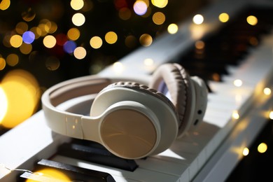 Photo of Headphones on electric piano against blurred lights, closeup. Bokeh effect