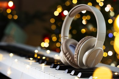 Photo of Headphones on electric piano against Christmas tree with blurred lights, closeup. Bokeh effect