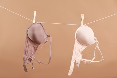 Photo of Beautiful bras hanging on rope against dark beige background