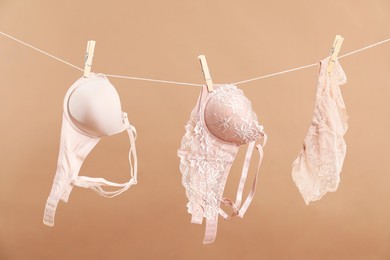 Photo of Beautiful bras and panties hanging on rope against dark beige background