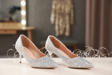 Elegant high heeled shoes and festive lights on white wooden table indoors