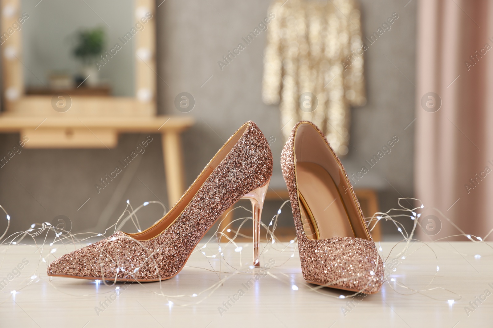 Photo of Elegant high heeled shoes and festive lights on white wooden table indoors