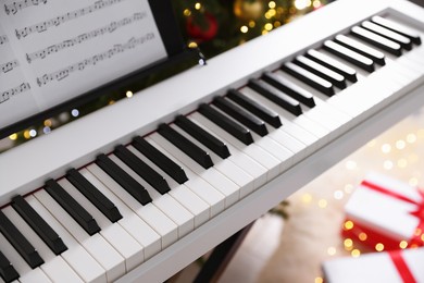 Photo of Synthesizer with music sheets near Christmas tree indoors, closeup