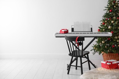 Photo of Synthesizer with music sheets and gift boxes near Christmas tree indoors, space for text