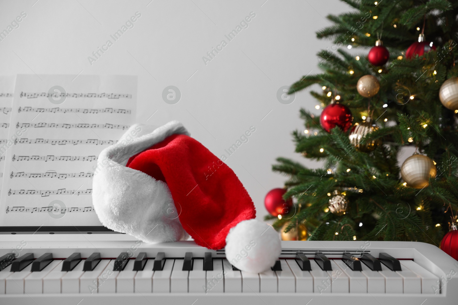 Synthesizer with music sheets and Santa hat near Christmas tree indoors, closeup Photo of Synthesizer with music sheets and Santa hat near Christmas tree indoors, closeup