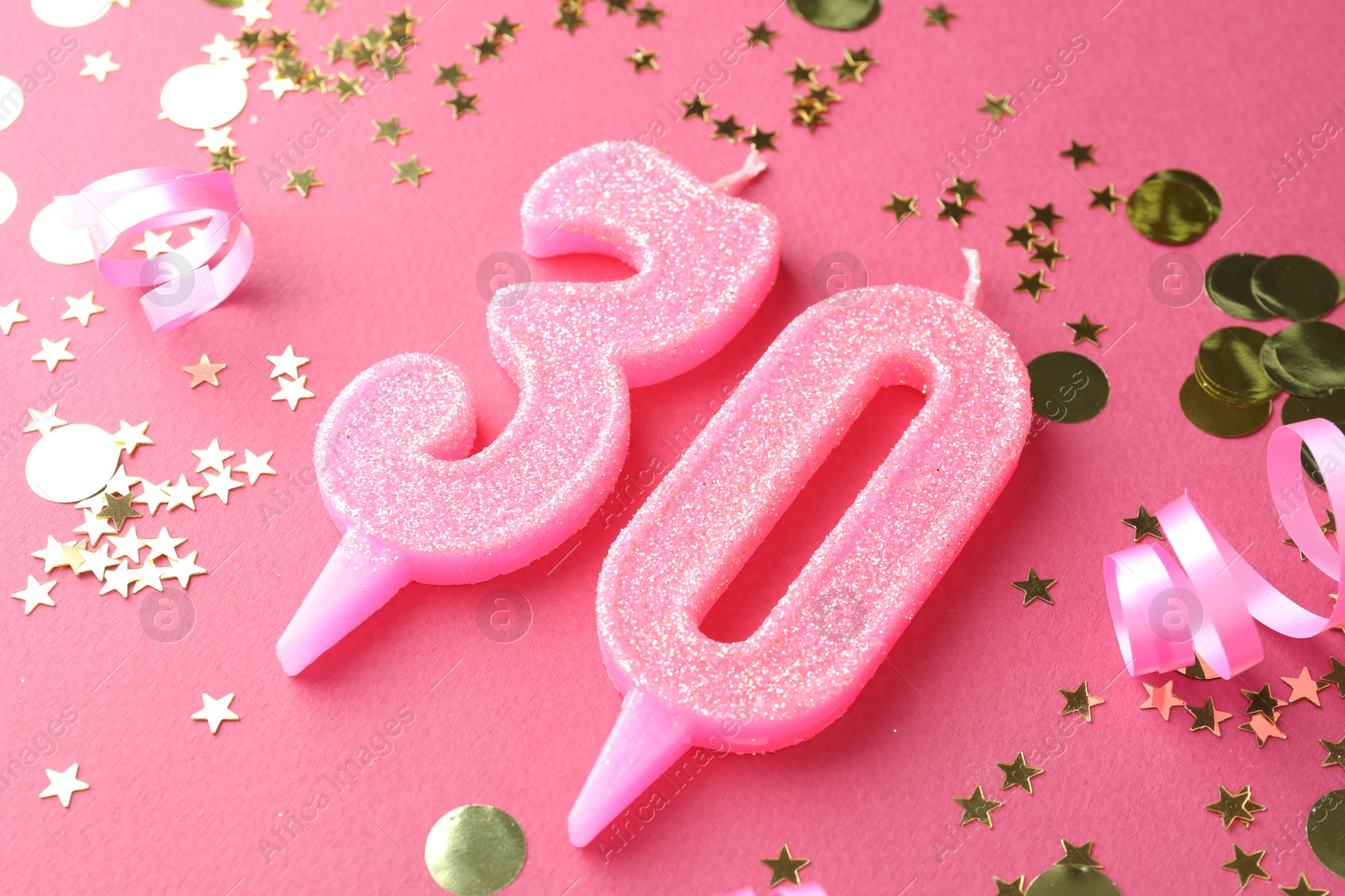 Photo of 30th birthday. Number shaped candles and confetti on pink background, closeup