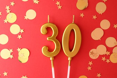 Photo of 30th birthday. Number shaped candles and confetti on red background, flat lay