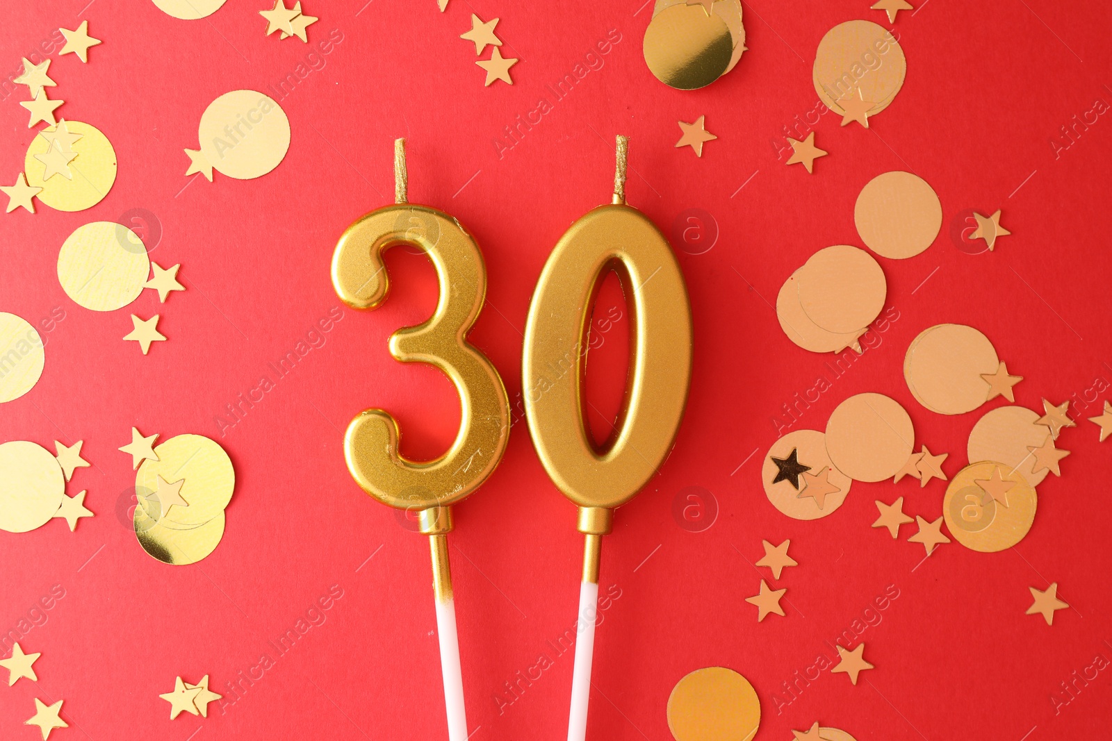 Photo of 30th birthday. Number shaped candles and confetti on red background, flat lay