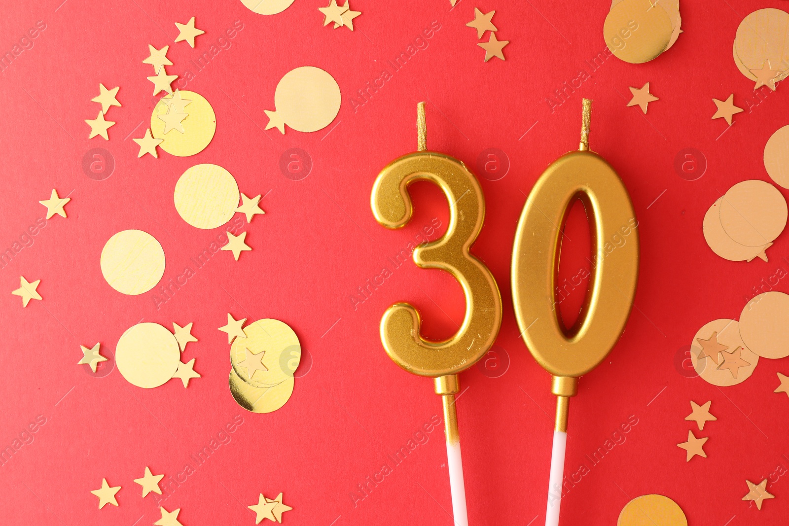 Photo of 30th birthday. Number shaped candles and confetti on red background, flat lay