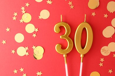 Photo of 30th birthday. Number shaped candles and confetti on red background, flat lay