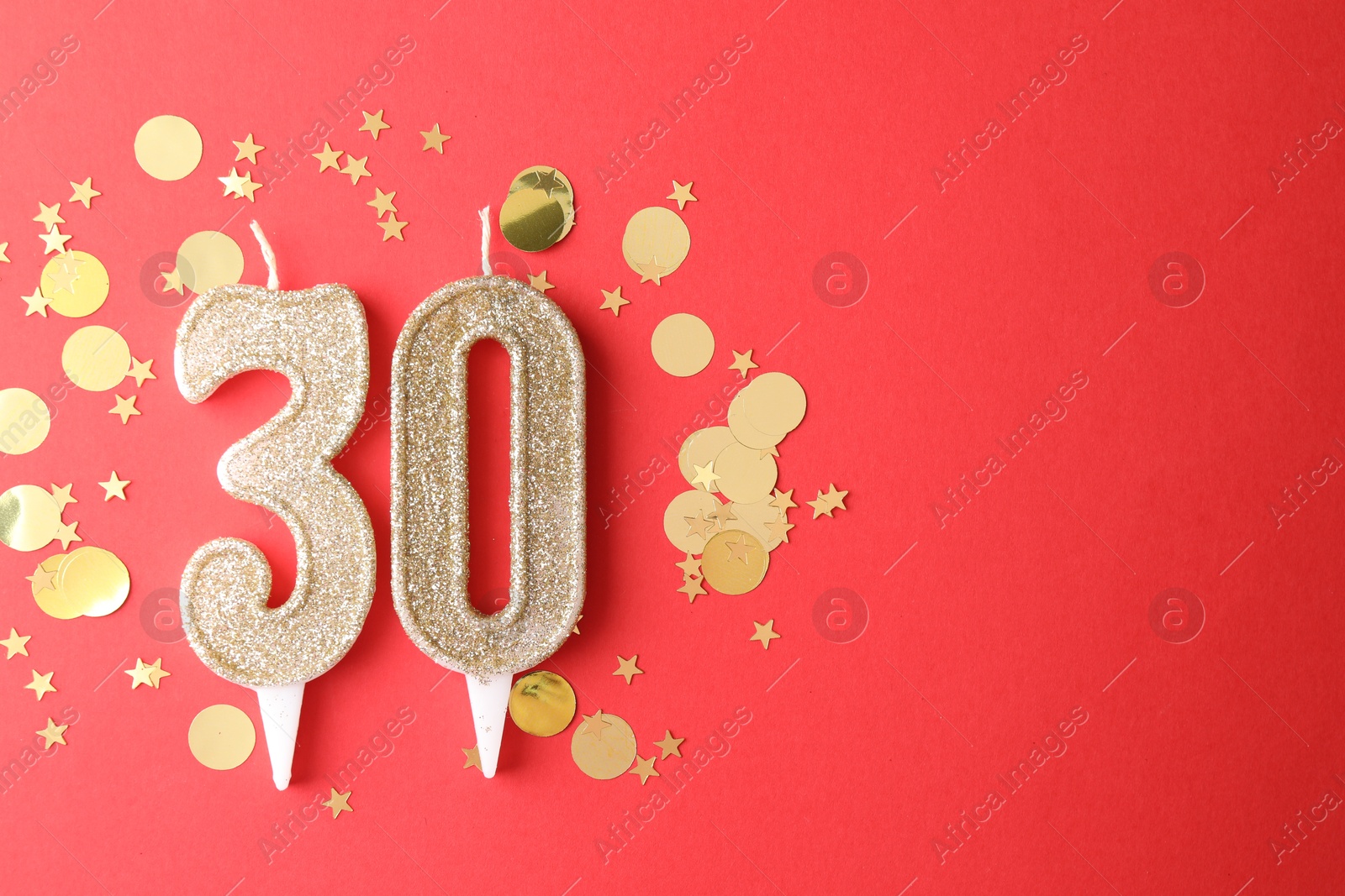 Photo of 30th birthday. Number shaped candles and confetti on red background, flat lay. Space for text