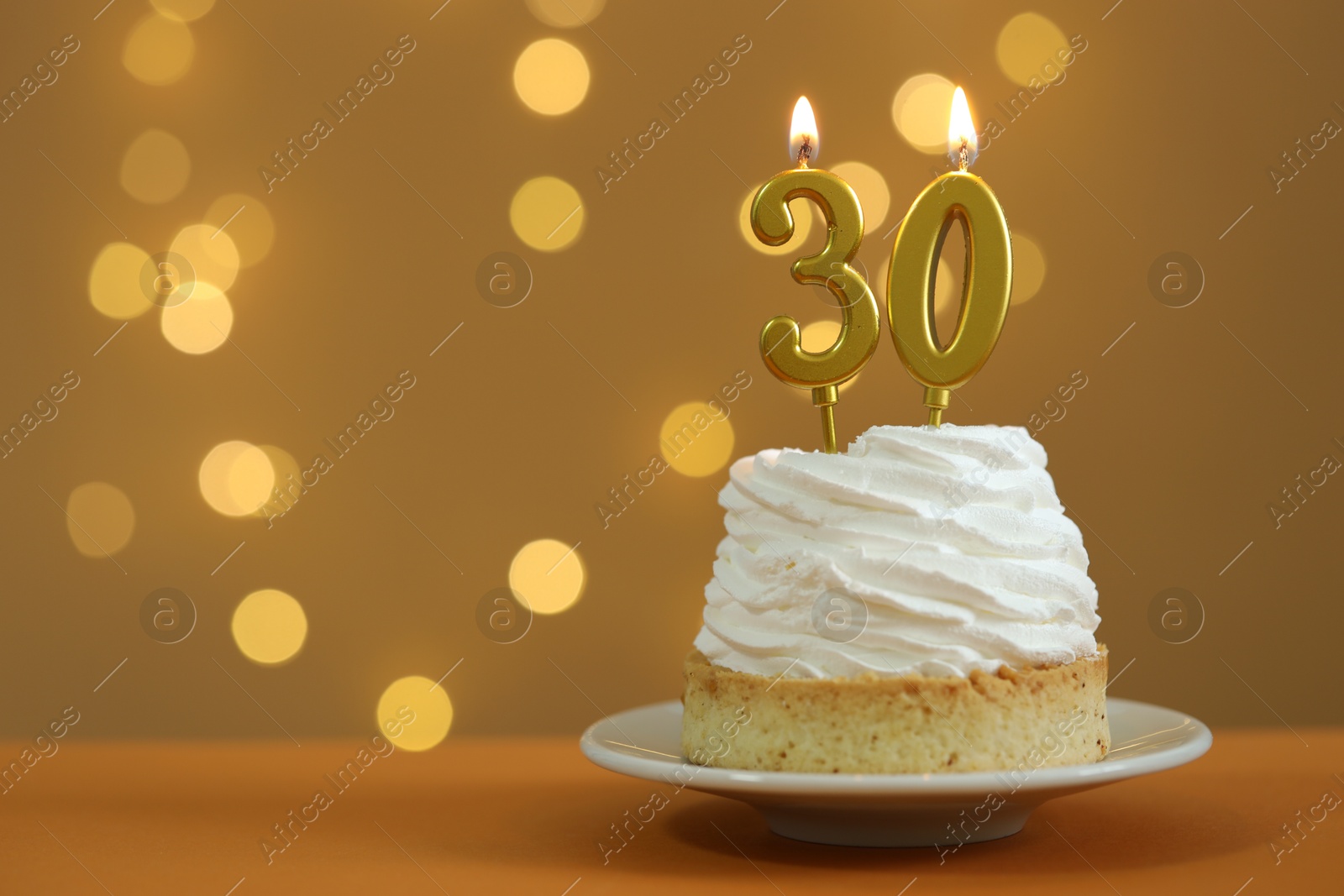 Photo of 30th birthday. Cupcake with burning number shaped candles on table against golden background with blurred lights, closeup and space for text. Bokeh effect