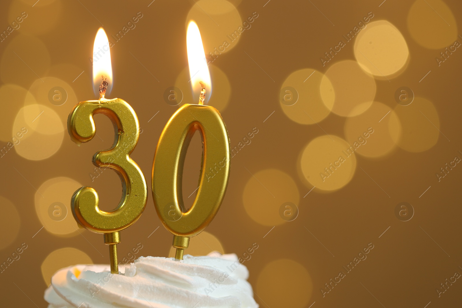 Photo of 30th birthday. Burning number shaped candles on cupcake against golden background with blurred lights, closeup and space for text. Bokeh effect