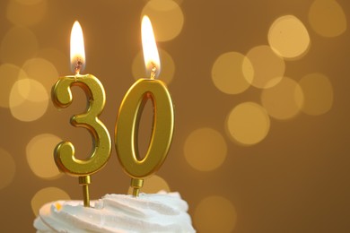 Photo of 30th birthday. Burning number shaped candles on cupcake against golden background with blurred lights, closeup and space for text. Bokeh effect