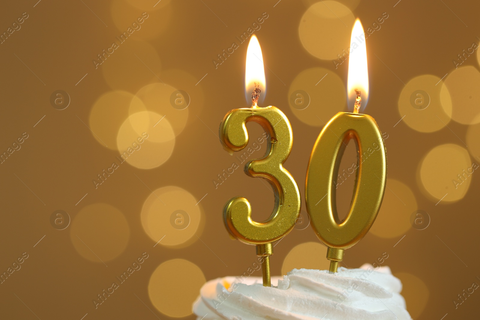 Photo of 30th birthday. Burning number shaped candles on cupcake against golden background with blurred lights, closeup and space for text. Bokeh effect