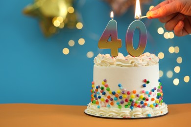 Photo of 40th birthday. Woman lighting number shaped candles on cake at table against blurred lights, closeup and space for text. Bokeh effect