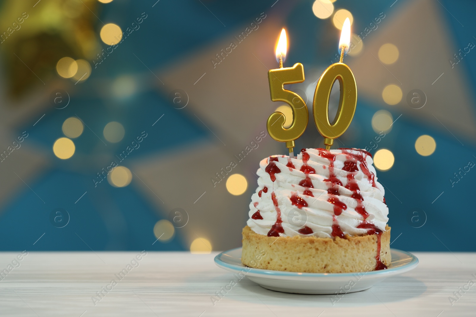 Photo of 50th birthday. Cupcake with burning number shaped candles on white wooden table against blurred background with lights, closeup and space for text. Bokeh effect