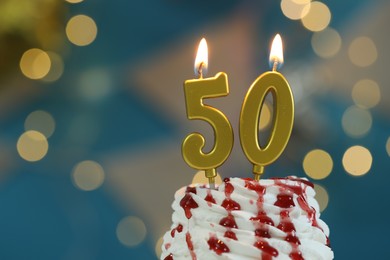 Photo of 50th birthday. Burning number shaped candles on cupcake against blurred background with lights, closeup. Bokeh effect