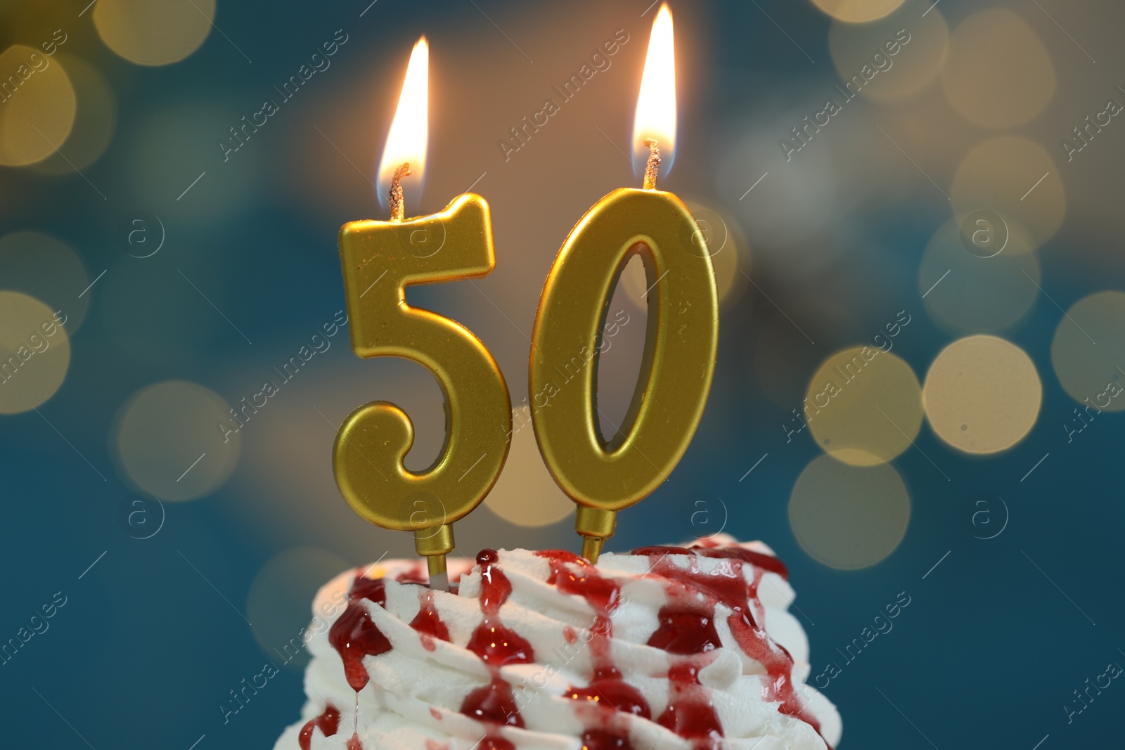 Photo of 50th birthday. Burning number shaped candles on cupcake against blurred background with lights, closeup. Bokeh effect