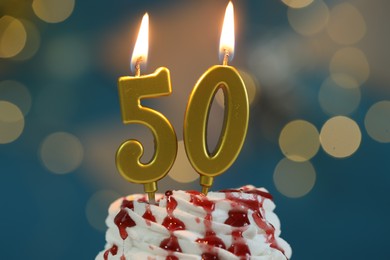 Photo of 50th birthday. Burning number shaped candles on cupcake against blurred background with lights, closeup. Bokeh effect