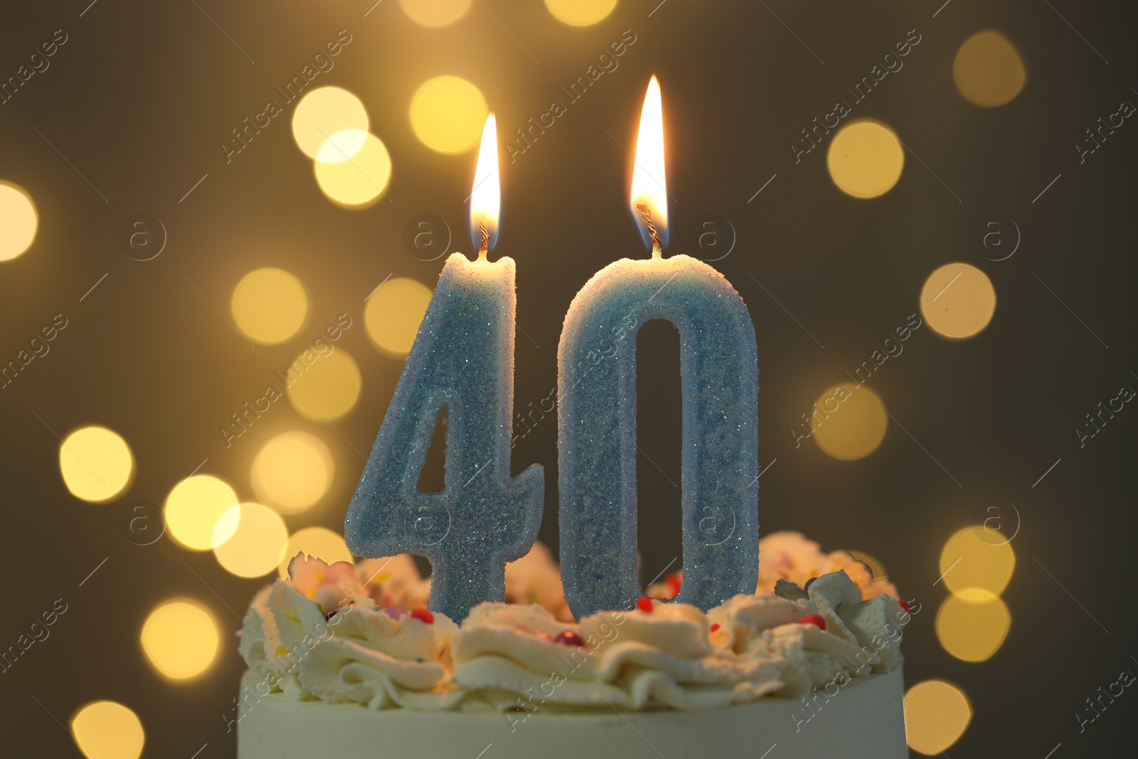 Photo of 40th birthday. Burning number shaped candles on cake against blurred background with lights, closeup. Bokeh effect