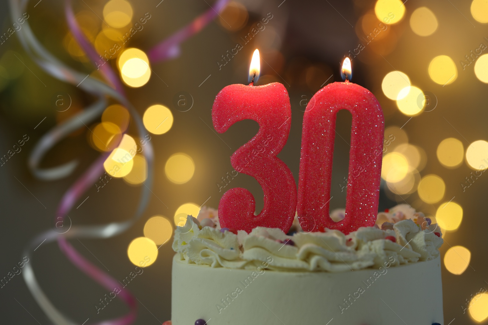 Photo of 30th birthday. Burning number shaped candles on cake against blurred background with lights, closeup. Bokeh effect