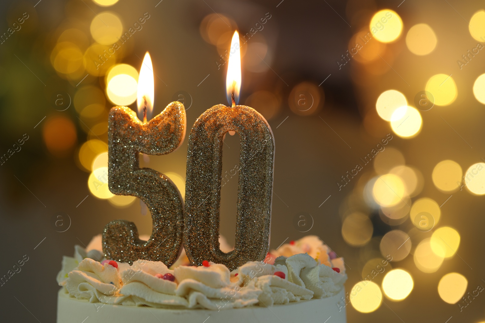 Photo of 50th birthday. Burning number shaped candles on cake against blurred background with lights, closeup and space for text. Bokeh effect