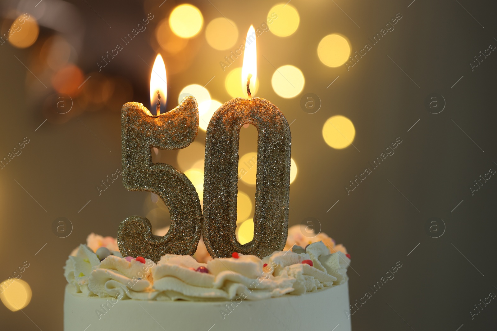 Photo of 50th birthday. Burning number shaped candles on cake against blurred background with lights, closeup and space for text. Bokeh effect