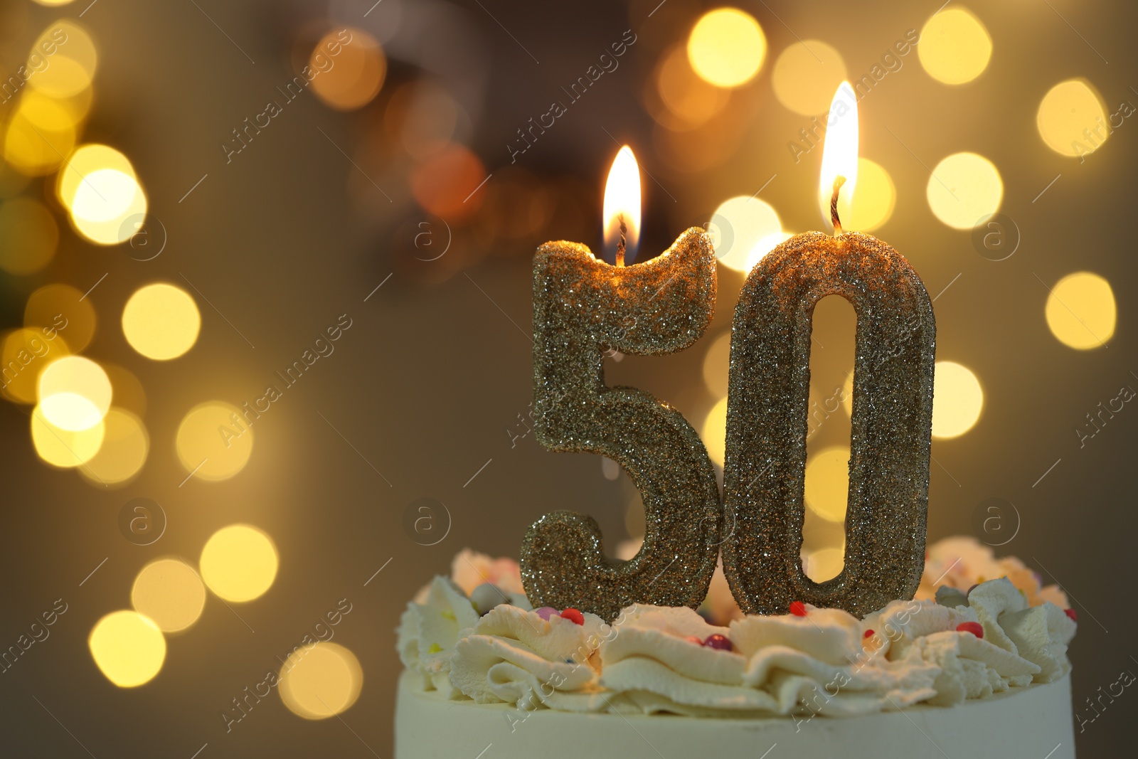 Photo of 50th birthday. Burning number shaped candles on cake against blurred background with lights, closeup and space for text. Bokeh effect